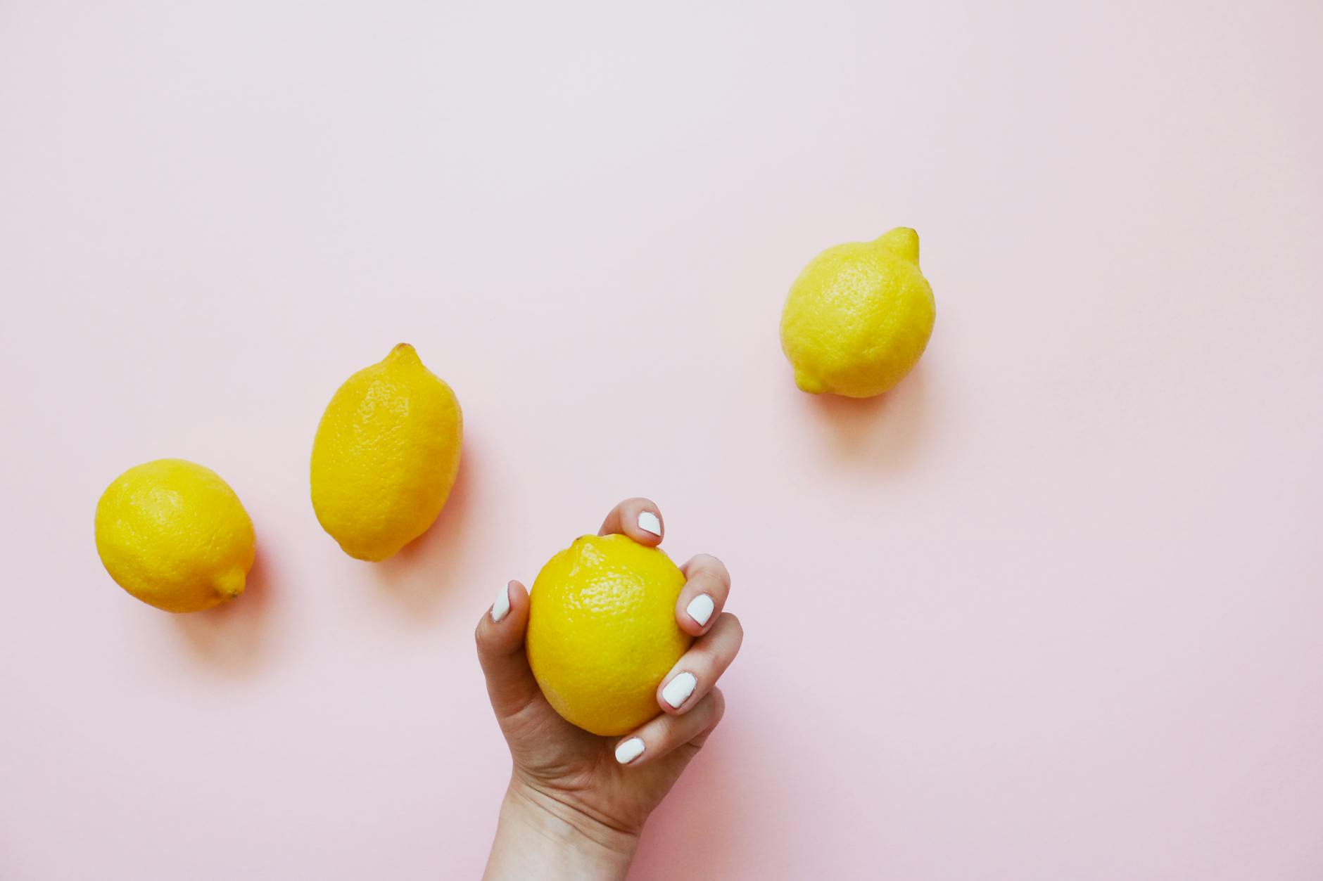 Hand holding fresh lemon on soft pink background with additional lemons nearby