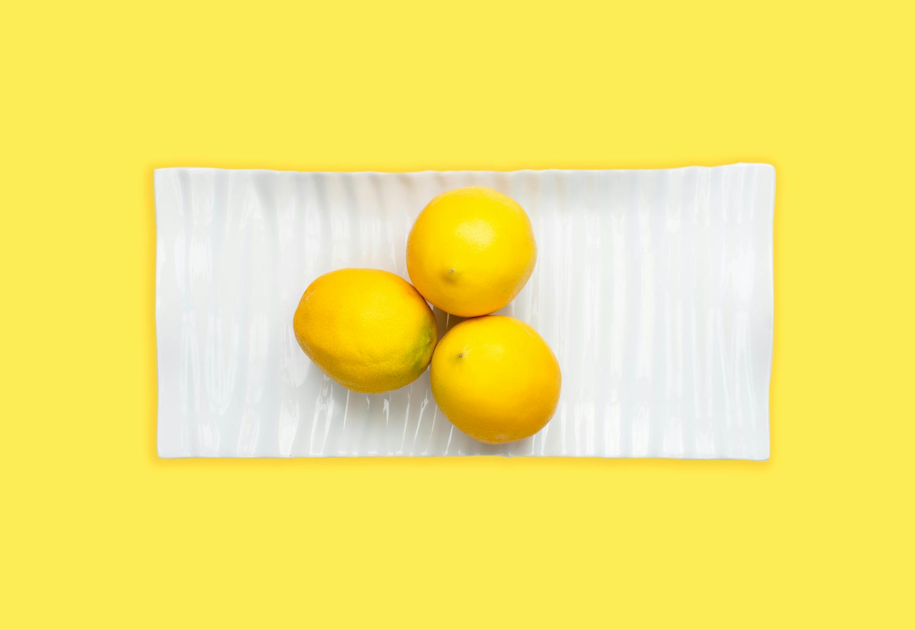 Hand with white nails holding a fresh lemon on soft pink background