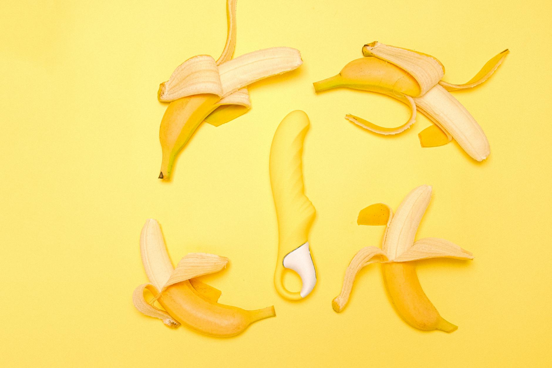 Yellow silicone lemon vibrator surrounded by fresh lemon halves on a bright yellow background