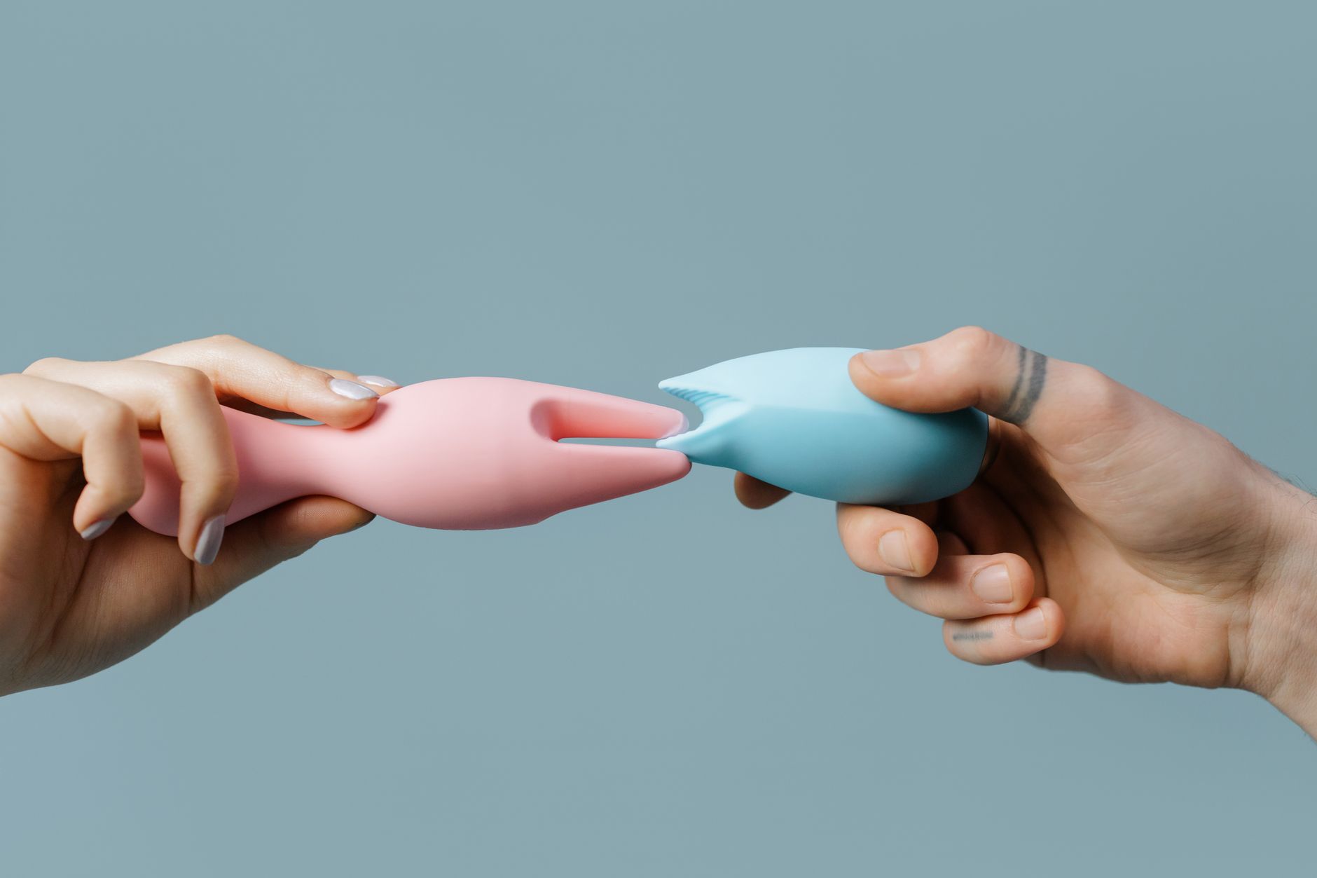 Woman holding blue and pink clitoral vibrators, contemplative and self-assured