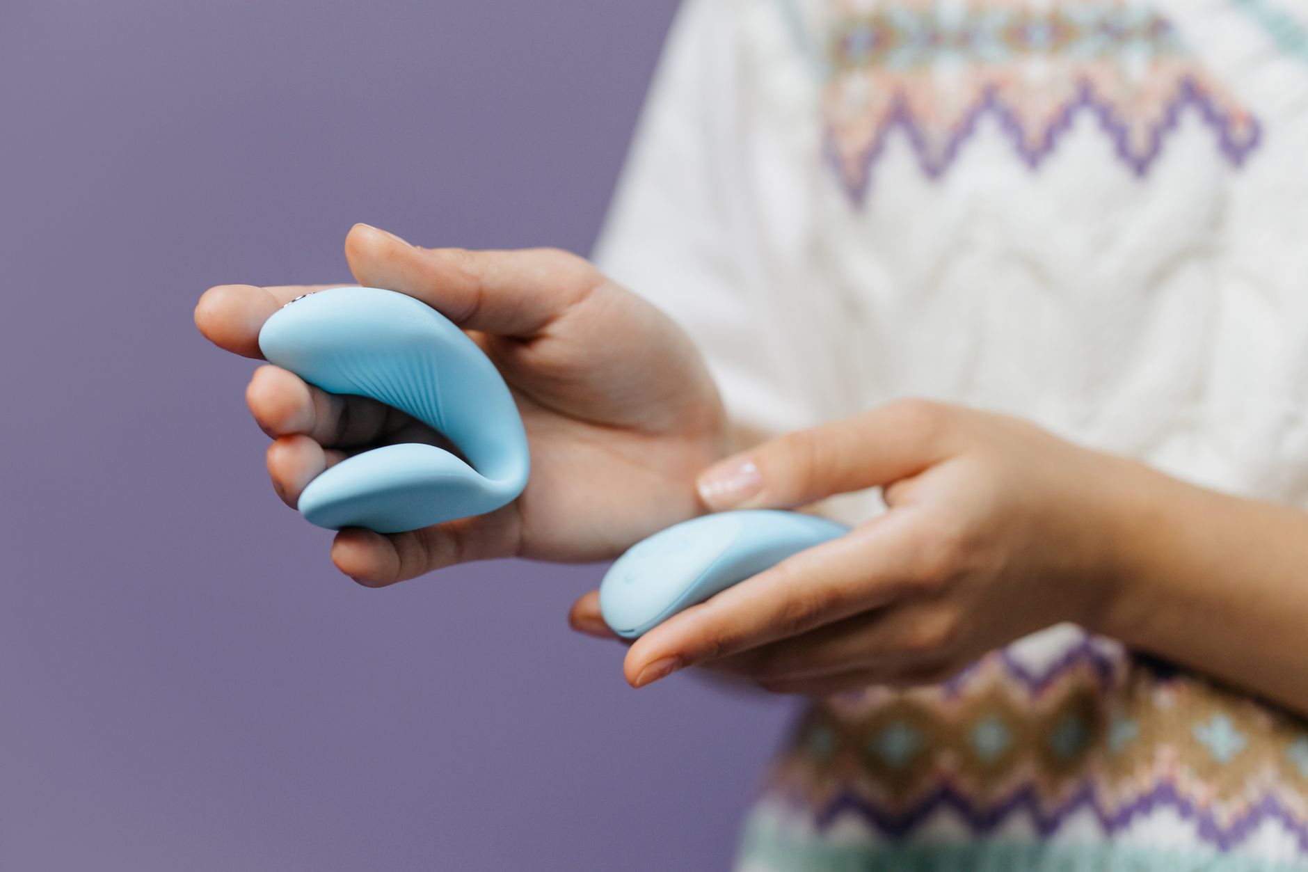 Close-up of hands holding a sleek blue vibrator against a purple background, representing gentle pleasure control.