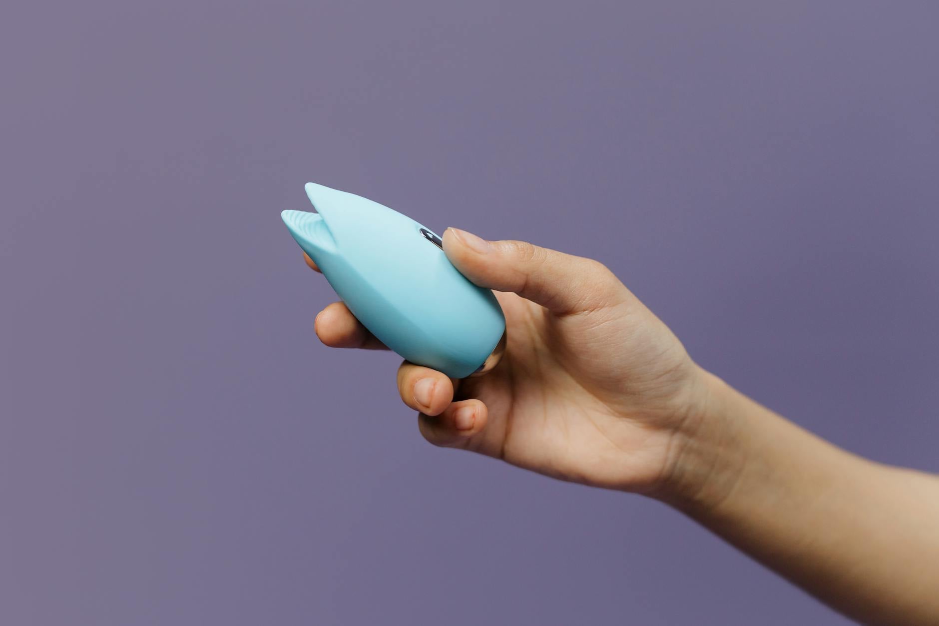 A hand holding a fresh lemon on a soft pink background